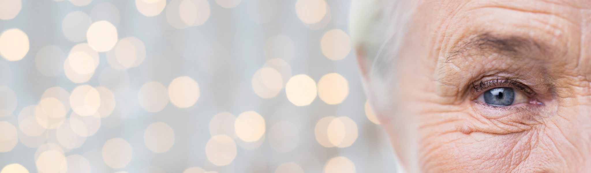 age, vision and old people concept - close up of senior woman face and eye over holidays lights background